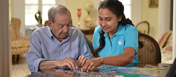 Home caregiver plays jigsaw puzzle with elderly man